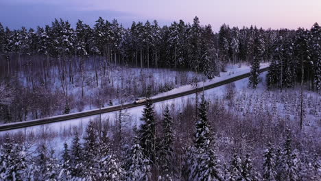 Cars-drive-on-road-in-bright-and-snowy-forest,-aerial-drone-shot