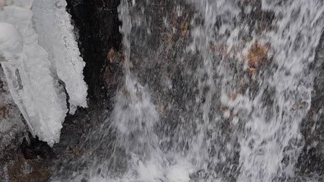 Vertically-moving-shot-of-a-small,-wild-waterfall-in-winter