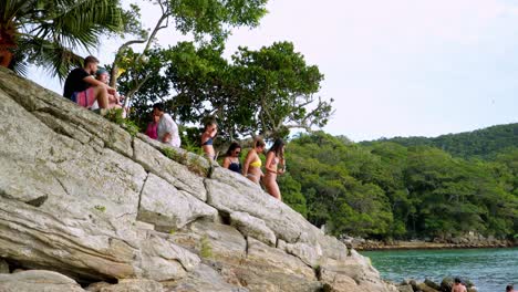 Menschen,-Die-An-Einem-Felsigen-Ufer-Sitzen,-Entspannen-Sich-Und-Machen-Selfies-In-Der-Nähe-Des-Meeres,-Umgeben-Von-Wald,-Praia-Da-Sepultura,-Brasilien