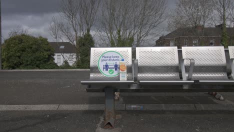 Close-up-of-a-coronavirus-sign-with-litter-on-a-metal-seat-at-a-quiet-train-station