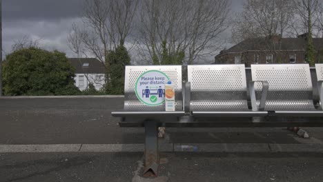 Primer-Plano-De-Un-Cartel-De-Coronavirus-Con-Basura-En-Un-Asiento-De-Metal-En-Una-Estación-De-Tren-Tranquila