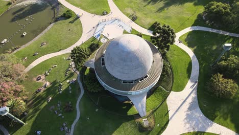 Aerial-lowering-on-Galileo-Galilei-Planetarium-between-paths-in-Palermo-Woods-at-daytime,-Buenos-Aires