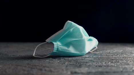 Blue-surgical-face-mask-in-white-on-a-table-with-black-background-filmed-on-a-slider