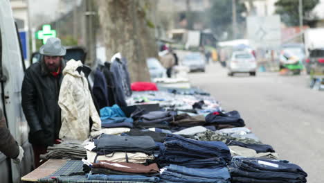 Mann,-Der-Tagsüber-Kleidungsstücke-Auf-Der-Straße-Mit-Verkehr-In-Der-Stadt-Leiria,-Portugal,-Verkauft