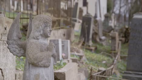 Little-Cute-Stone-Angel-Praying-in-front-of-Tombstone-with-Graveyard-in-Background