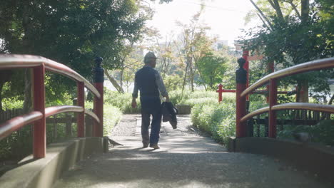Rückansicht-Eines-Alten-Japanischen-Mannes,-Der-Allein-Im-Park-Spazieren-Geht,-Während-Tauben-Auf-Dem-Boden-Suchen