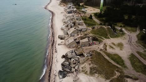 Aerial-view-of-abandoned-seaside-fortification-building-at-Karosta-Northern-Forts-on-the-beach-of-Baltic-sea-in-Liepaja-in-overcast-spring-day,-wind-turbine,-wide-drone-shot-moving-backwards,-tilt-up