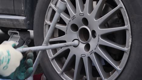 Close-up-worker-with-gloves-fixes-wheel-with-cross-wrench-and-nuts