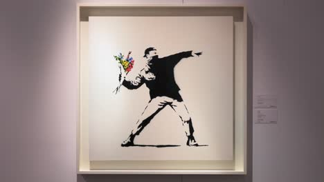 Banksy-Kunstwerk-Mit-Dem-Namen-„Love-Is-In-The-Air“,-Das-Einen-Demonstranten-Darstellt,-Der-Auf-Frischer-Tat-Dabei-Ertappt-Wird,-Wie-Er-Einen-Strauß-Bunter-Blumen-Anstelle-Eines-Molotow-Cocktails-Auf-Einer-Sotheby&#39;s-Show-In-Hongkong-Schleudert