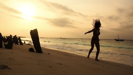 Tracking-shot-of-girl-walking-on-beach-in-Zanzibar-during-sunset,-jumping-for-joy