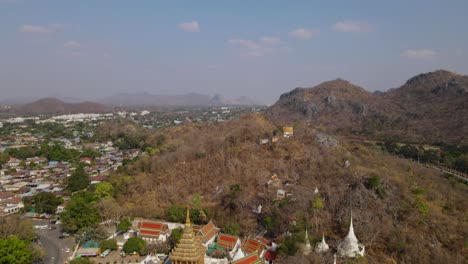 Wat-Phra-Phutthabat,-Saraburi,-Thailand,-4k-aerial-tilt-footage-from-the-temple-complex-to-the-the-horizon-revealing-a-road-on-the-left-side,-communities-and-limestone-hills