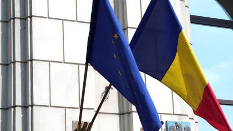 Slowmo-gimbal-shot-of-Romanian-and-European-Union-flags-waving-in-wind