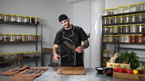 Young-tattooed-chef-in-a-black-apron-sharpening-a-knife-in-the-kitchen