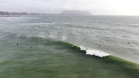 4k-aerial-video-shot-during-daytime-of-a-surfer-catching-and-riding-a-wave-on-the-coastal-waters-of-the-Pacific-ocean-in-Lima,-Peru