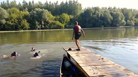 Glückliche-Kinder,-Die-In-Der-Nähe-Des-Flussufers-Spielen-Und-Von-Der-Mole-In-Den-Fluss-Springen