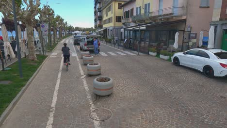 Ungewöhnliche-Und-Einzigartige-Rückansicht-Einer-Frau,-Die-Fahrrad-Entlang-Der-Uferpromenade-Von-Arona-In-Italien-Fährt