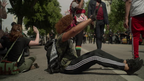 Hombre-Afroamericano-Sentado-En-El-Suelo-Con-Las-Manos-En-Alto-Frente-A-Los-Agentes-De-Policía-En-Una-Cámara-Lenta-De-Protesta-Disparada-En-Cámara-Roja-4k