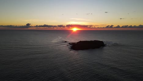 Hochschwenkende-Drohnenansicht-Eines-Farbenfrohen-Morgensonnenaufgangs-Hinter-Einer-Silhouette-Einer-Meeresparkinsel