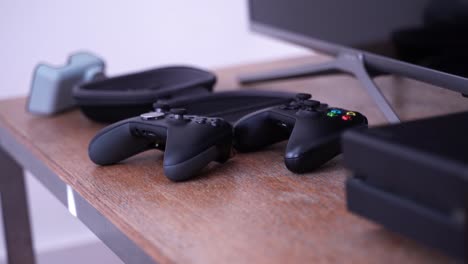 Two-Xbox-One-videogame-controllers-and-console-on-a-table,-medium-shot-zoom-in