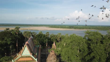 Hermosa-Pagoda-Con-Pájaros-En-Cámara-Lenta-Volando,-Al-Lado-Del-Pintoresco-Río-Mekong