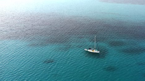 White-Sailboat-Anchored-On-Clear-Blue-Water-Of-Ocean-Near-The-Bahamas-In-Summer