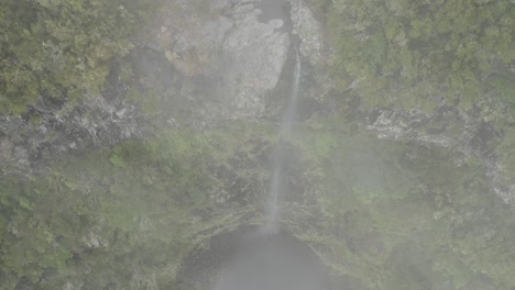 Drone-shot-moving-down-through-thin-clouds,-revealing-Lagoa-da-Vento-waterfall-in-Madeira