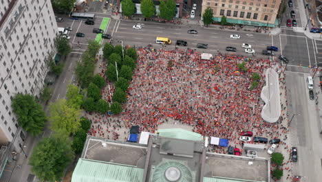 Huge-crowd-of-Native-protesters-assemble-below,-pan-orbit-aerial-from-high-above