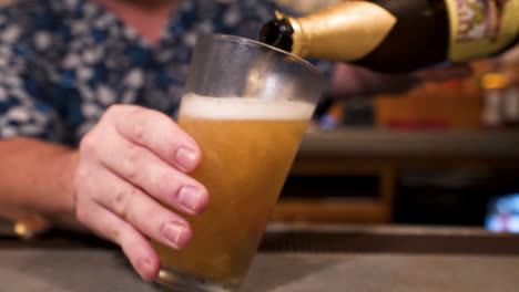 Barkeeper-Gießt-Schwer-Flasche-Bier-In-Mattiertes-Pintglas,-Schieberegler-In-Zeitlupe-Hd