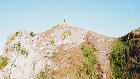 Aerial-shot-flying-towards-man-standing-on-top-of-Thor's-Cave,-Ashbourne,-Peak-District