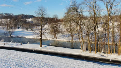 Schnee-Aus-Der-Luft,-Der-über-Die-Wasserstraße-Mit-Blattlosen-Bäumen-Und-Weißen-Ufern-Fällt
