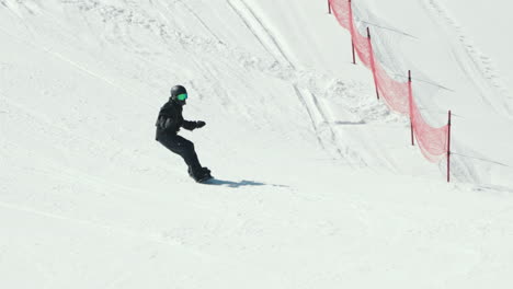 Tiro-De-Dron-De-Un-Snowboarder-Aficionado-Con-Ropa-De-Esquí-Negra-Haciendo-Snowboard-Cuesta-Abajo-En-Un-Día-De-Invierno-Frío-Y-Brillante,-Tiro-De-Seguimiento