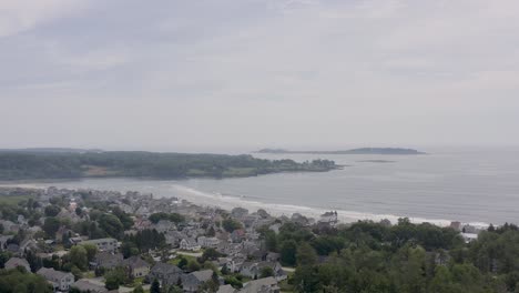 Drohnenaufnahme-Einer-Strandgemeinde-In-Maine,-Die-über-Die-Häuser-Mit-Menschen-Am-Strand-Im-Hintergrund-Geht