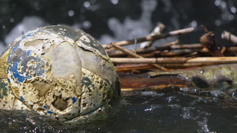 Old-rotten-soccer-football-swimming-on-water-surface-of-lake,close-up-shot-in-4k