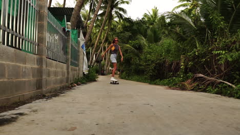 Beautiful-and-cute-young-caucasian-girl-riding-the-skateboard-on-the-road-between-the-palm-trees-and-suburb-houses---low-angle-dolly-shot