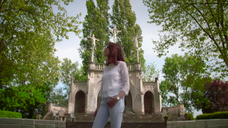 Young-beautiful-woman-with-sunglasses-standing-and-looking-around-in-front-of-a-calvary-surrounded-by-a-forest
