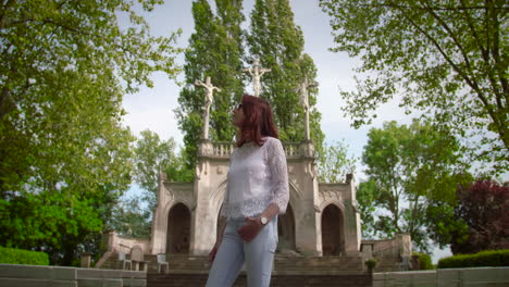 Mujer-Hermosa-Joven-Con-Gafas-De-Sol-De-Pie-Y-Mirando-A-Su-Alrededor-Frente-A-Un-Calvario-Rodeado-Por-Un-Bosque