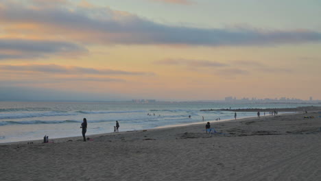 Leute,-Die-Sonnenuntergang-Und-Meereswellen-Am-Imperial-Beach-In-Kalifornien-Mit-Der-Skyline-Von-San-Diego-In-Der-Ferne-Genießen