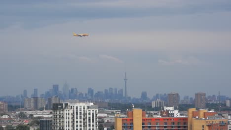 Tracking-shot-of-an-airplane-flying-across-the-sky-with-downtown-cityscape-in-the-background-at-Toronto-Pearson-International-Airport,-Mississauga,-Ontario,-Canada