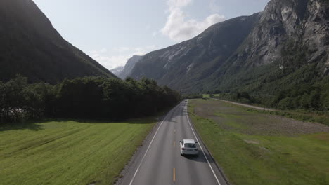 Conducción-De-Automóviles-En-Una-Carretera-Rural-Con-Un-Valle-Escénico-En-El-Fondo-En-Romsdalen,-Noruega---Toma-Aérea-De-Drones