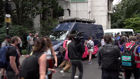 Los-Manifestantes-Marchan-Frente-A-Una-Camioneta-Azul-Con-Una-Cámara-De-Vigilancia-De-Reconocimiento-Facial-En-El-Techo-Durante-Una-Rebelión-De-Extinción-Protesta-Por-El-Cambio-Climático