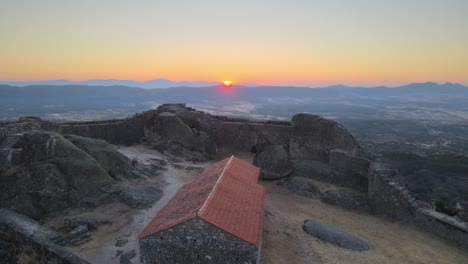 Cinematic-aerial-forward-over-Monsanto-ruins-while-sun-rises-on-horizon,-Portugal