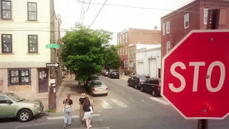 Aerial-view-rising-above-stop-sign-as-three-young-females-cross-pedestrian-street-crossing-in-south-Philadelphia