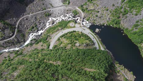 Crazy-good-descending-aerial-over-Mabodalen-mountain-road-leading-to-Hardangervidda-national-park-Norway---180-degree-U-turn-curve-from-one-tunnel-to-another---Lake-with-river-and-forest-surroundings
