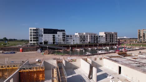 Movimiento-Aéreo-Hacia-Atrás-Que-Muestra-El-Sitio-De-Construcción-Del-Complejo-Kade-Zuid-De-Apartamentos-De-Lujo-Que-Se-Está-Construyendo-En-Una-Antigua-Zona-Industrial-Con-Kade-Noord-Terminado-Detrás-Del-Puerto-Recreativo-En-El-Fondo