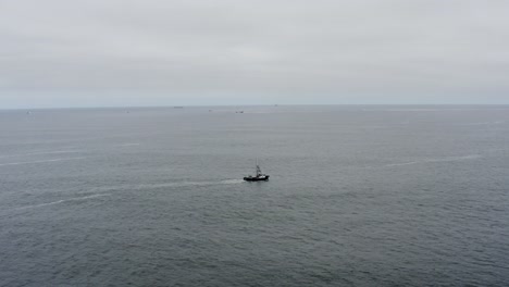 Drone-aerial-tracking-alongside-a-lone-fishing-boat-going-out-to-see-on-a-cloudy-and-calm-day