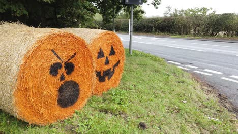 Spooky-orange-painted-hay-bale-Halloween-pumpkin-decoration-on-rural-farm-road
