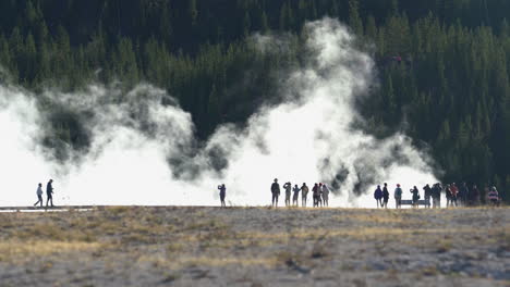 Visitantes-En-El-Parque-Nacional-De-Yellowstone-Caminando-Por-El-Camino-De-Manantiales-Geotérmicos-Y-Piscinas-Calientes-Con-Vapor-En-El-Fondo,-Marco-Completo