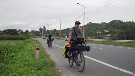 Reisende-Mit-Fahrrädern-Fahren-Am-Straßenrand-Entlang,-Während-Motorräder-Und-Autos-Vorbeifahren