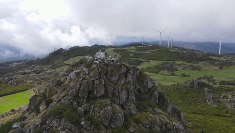 Aerial-circling-around-Caramulinho-mount-nd-wind-turbines-for-eolic-energy-production-in-background,-Portugal