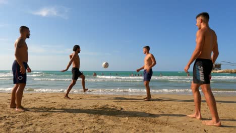 Group-of-guys-have-fun-playing-soccer-on-sandy-beach-at-Punta-Penna-in-Abruzzo,-Italy